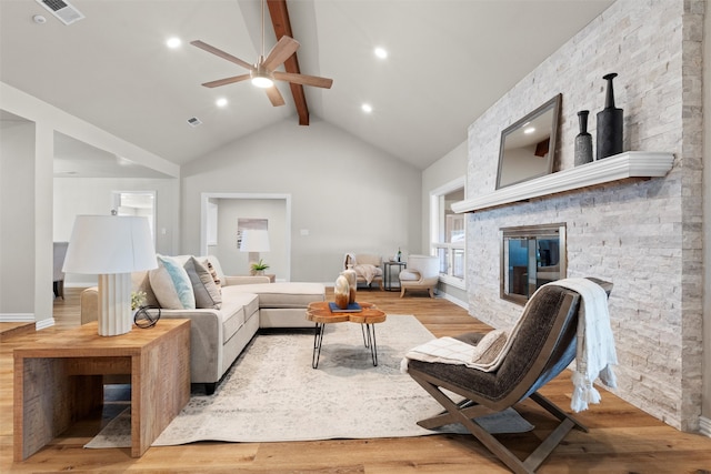 living room with a fireplace, beamed ceiling, high vaulted ceiling, ceiling fan, and light wood-type flooring