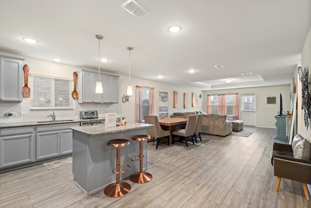 kitchen featuring a center island, sink, gray cabinetry, light wood-type flooring, and decorative light fixtures