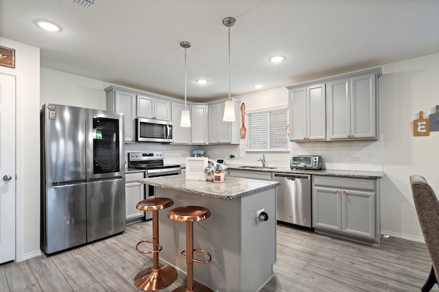 kitchen featuring light stone counters, appliances with stainless steel finishes, pendant lighting, a kitchen island, and light wood-type flooring