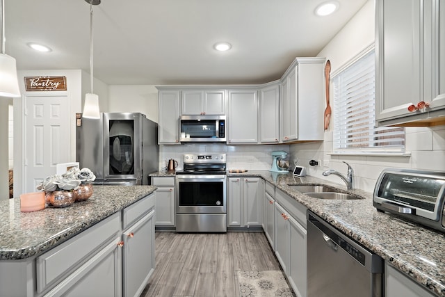 kitchen featuring sink, appliances with stainless steel finishes, light stone countertops, light hardwood / wood-style flooring, and pendant lighting