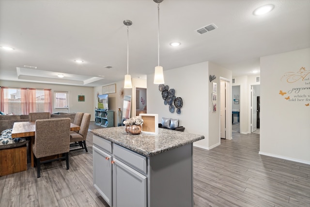 kitchen featuring light hardwood / wood-style flooring, decorative light fixtures, a kitchen island, and light stone countertops