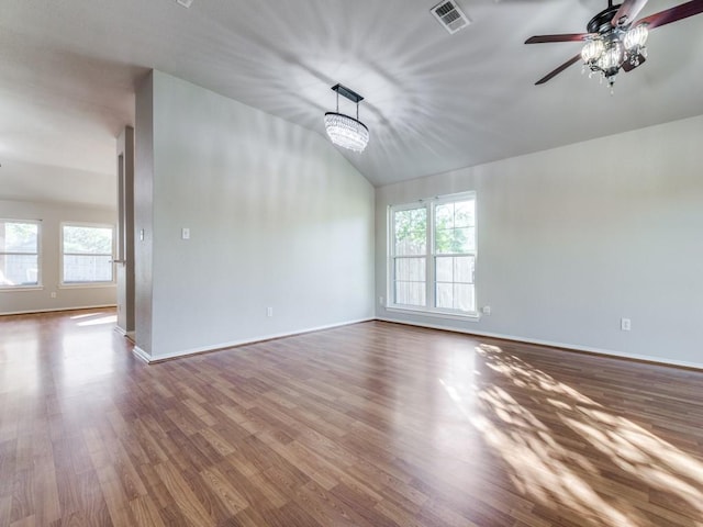 empty room with hardwood / wood-style floors, ceiling fan with notable chandelier, a wealth of natural light, and lofted ceiling