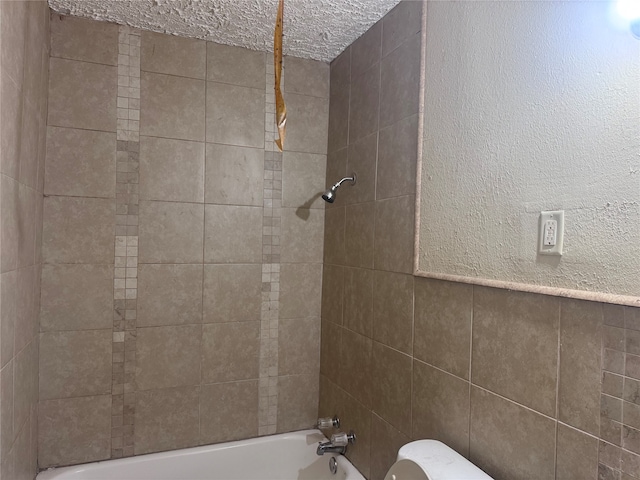 bathroom with tiled shower / bath, a textured ceiling, and toilet