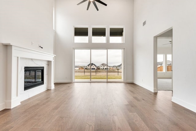 unfurnished living room featuring wood-type flooring, a towering ceiling, ceiling fan, and a premium fireplace