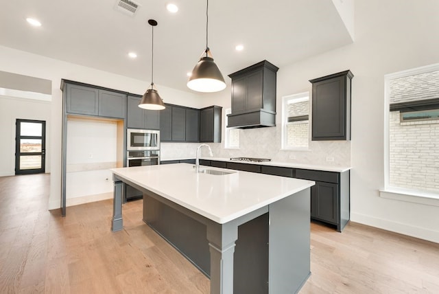 kitchen with a wealth of natural light, custom exhaust hood, a kitchen island with sink, and sink