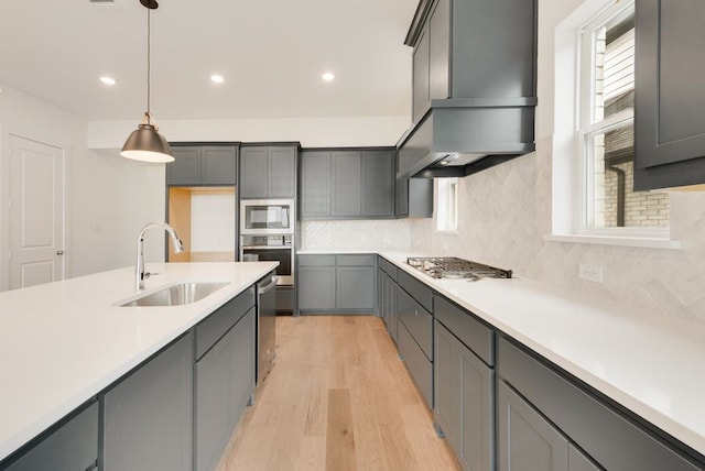 kitchen with sink, hanging light fixtures, wall chimney range hood, backsplash, and appliances with stainless steel finishes