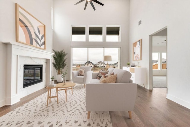 living room with ceiling fan, wood-type flooring, a high ceiling, and a premium fireplace