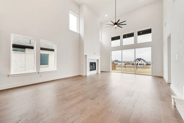 unfurnished living room featuring a fireplace, a high ceiling, light hardwood / wood-style flooring, and ceiling fan