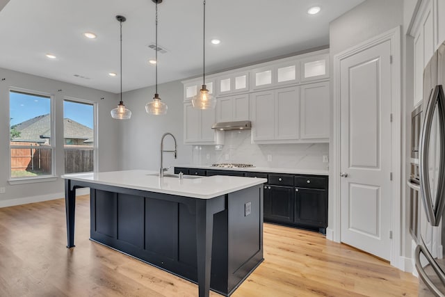 kitchen featuring an island with sink, sink, white cabinets, backsplash, and hanging light fixtures