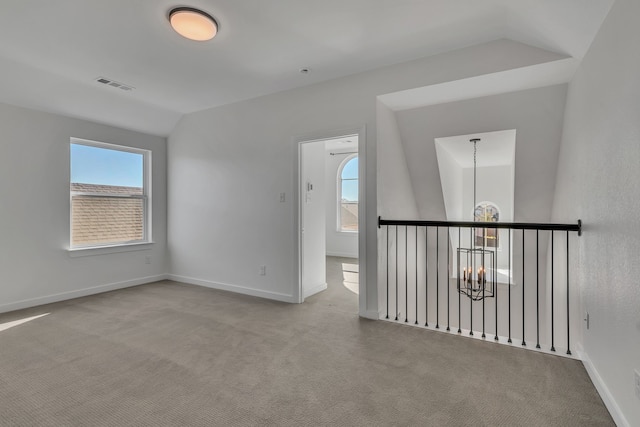 spare room with an inviting chandelier, light colored carpet, and vaulted ceiling