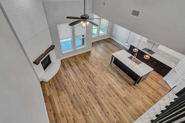 unfurnished living room with ceiling fan, sink, light hardwood / wood-style flooring, and high vaulted ceiling