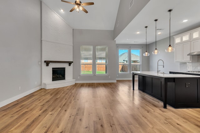 kitchen featuring pendant lighting, stainless steel gas stovetop, white cabinetry, sink, and a kitchen island with sink