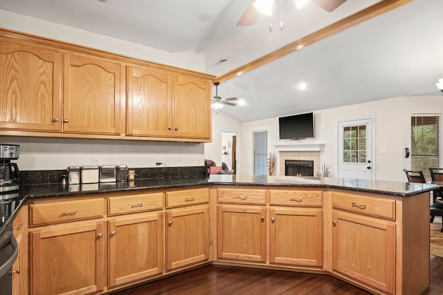 kitchen featuring kitchen peninsula, dark stone counters, dark hardwood / wood-style floors, a tile fireplace, and lofted ceiling with beams