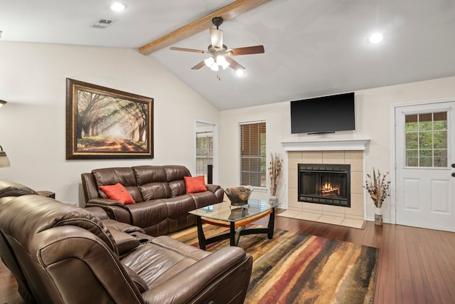 living room featuring ceiling fan, a tiled fireplace, dark hardwood / wood-style flooring, and lofted ceiling with beams