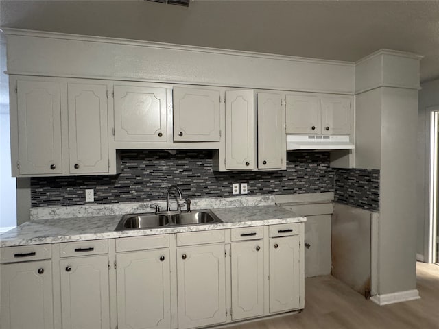 kitchen with tasteful backsplash, white cabinets, sink, and light hardwood / wood-style flooring