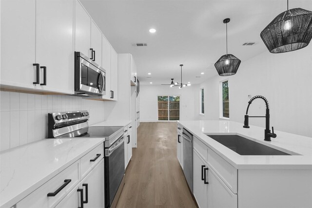 kitchen with white cabinetry, hanging light fixtures, sink, and stainless steel appliances