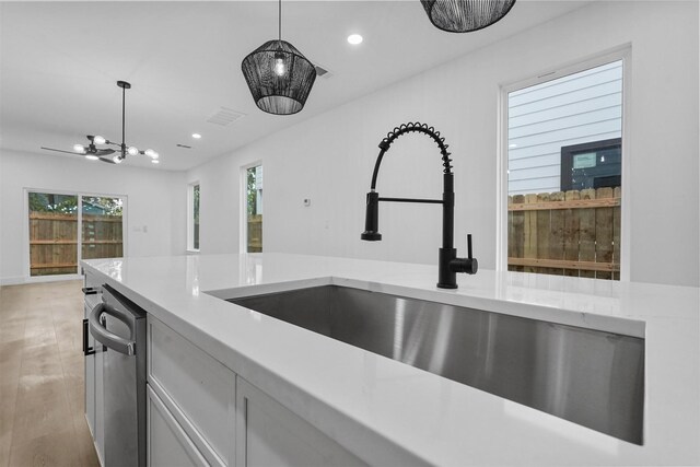 kitchen with white cabinets, light wood-type flooring, hanging light fixtures, and sink