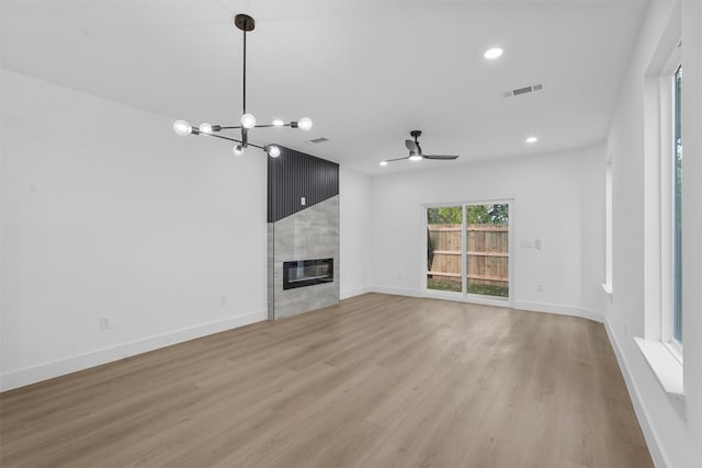 unfurnished living room featuring a tiled fireplace, ceiling fan with notable chandelier, and light hardwood / wood-style flooring