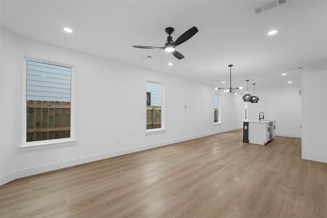 unfurnished living room featuring light hardwood / wood-style floors, ceiling fan with notable chandelier, and sink