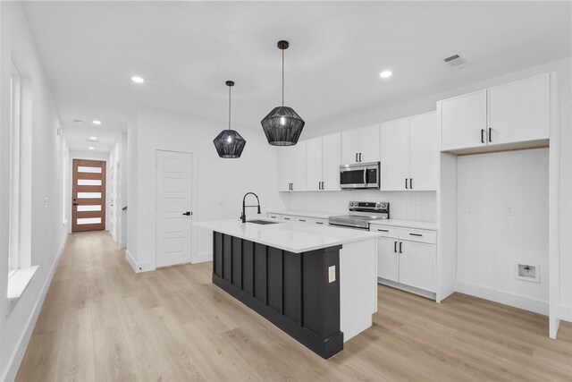 kitchen featuring sink, appliances with stainless steel finishes, an island with sink, hanging light fixtures, and light wood-type flooring