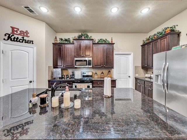 kitchen with dark brown cabinetry, sink, backsplash, dark stone counters, and appliances with stainless steel finishes