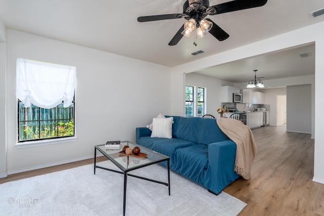 living room featuring light wood-type flooring and ceiling fan with notable chandelier