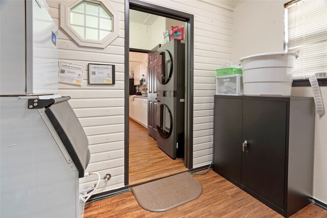 laundry room featuring stacked washer / dryer, light wood-type flooring, and wood walls