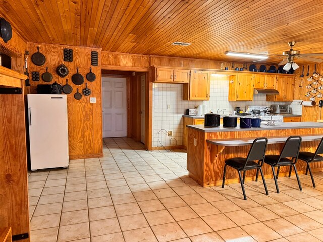 kitchen with light tile patterned flooring, a kitchen breakfast bar, decorative backsplash, white fridge, and wood ceiling