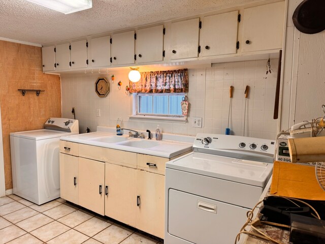 clothes washing area with sink, light tile patterned floors, washer and clothes dryer, cabinets, and a textured ceiling