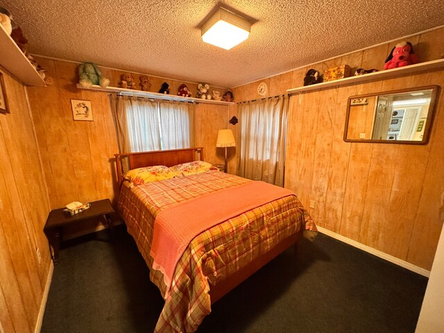 bedroom featuring dark colored carpet, a textured ceiling, and wood walls