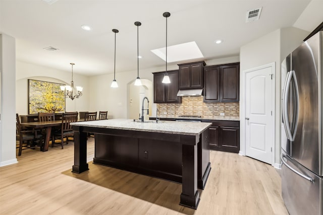 kitchen featuring stainless steel appliances, decorative light fixtures, dark brown cabinetry, sink, and a kitchen island with sink