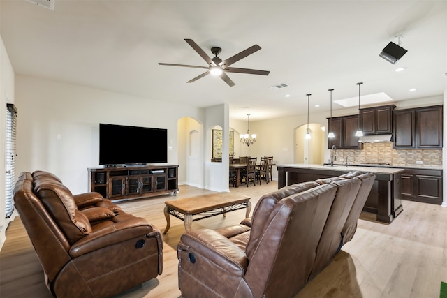 living room with light wood-type flooring, sink, and ceiling fan with notable chandelier