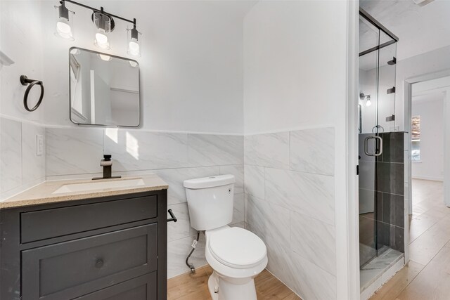 full bathroom with toilet, wood finished floors, vanity, a shower stall, and tile walls