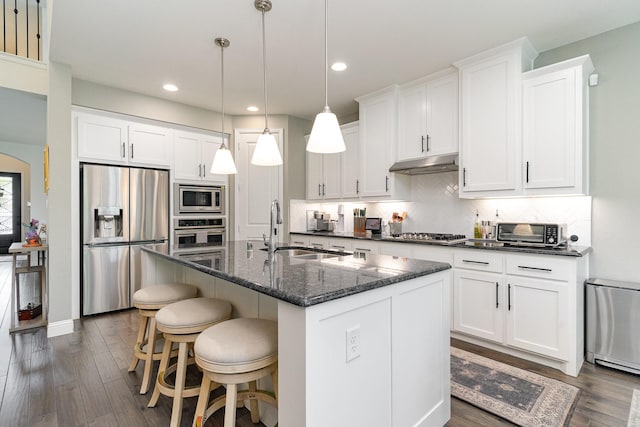 kitchen featuring white cabinetry, appliances with stainless steel finishes, hanging light fixtures, and a center island with sink