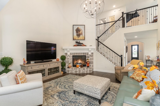 living room featuring a notable chandelier, wood-type flooring, a towering ceiling, and a fireplace