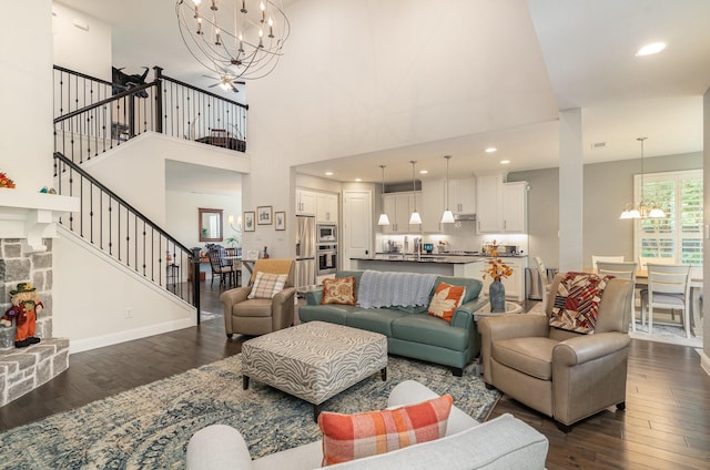 living room featuring a stone fireplace, dark hardwood / wood-style flooring, a high ceiling, and an inviting chandelier