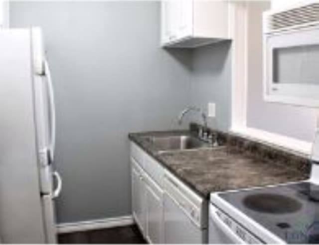 kitchen featuring dark stone counters, stove, white cabinetry, and sink