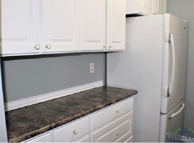 kitchen featuring white cabinets, dark stone countertops, and white refrigerator