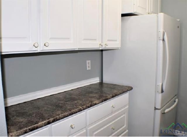 kitchen with white refrigerator, dark stone counters, and white cabinets