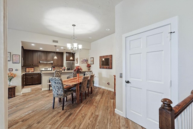 dining space with light hardwood / wood-style floors and a notable chandelier