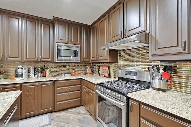 kitchen featuring light stone countertops, light hardwood / wood-style flooring, appliances with stainless steel finishes, and tasteful backsplash