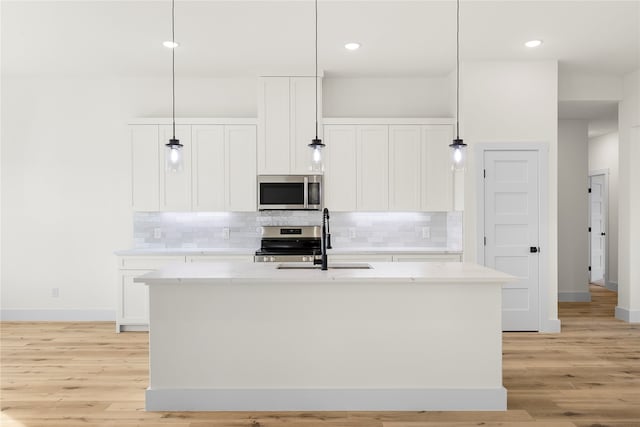 kitchen featuring sink, stainless steel appliances, hanging light fixtures, and an island with sink