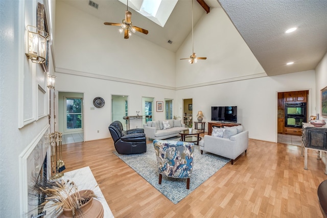 living area featuring lofted ceiling with skylight, visible vents, ceiling fan, and wood finished floors