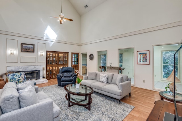 living area with light wood-type flooring, ceiling fan, a fireplace, and vaulted ceiling