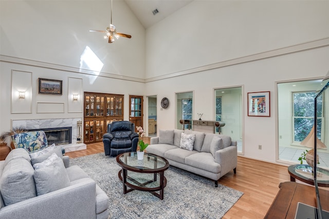 living room with high vaulted ceiling, ceiling fan, light hardwood / wood-style floors, and a fireplace