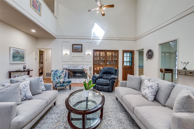 living room with hardwood / wood-style floors, a high ceiling, a high end fireplace, and ceiling fan