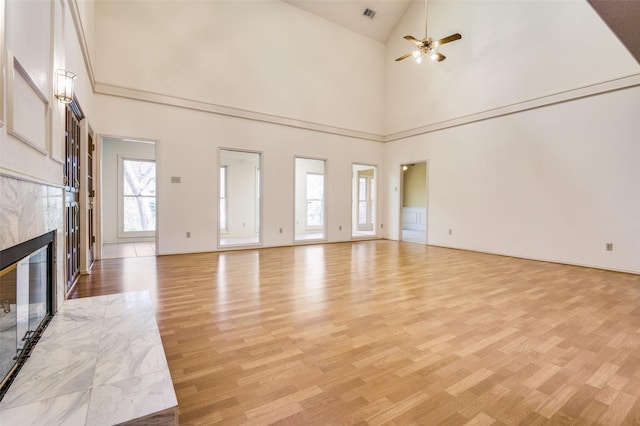 unfurnished living room with a tiled fireplace, light wood-style floors, visible vents, and a ceiling fan