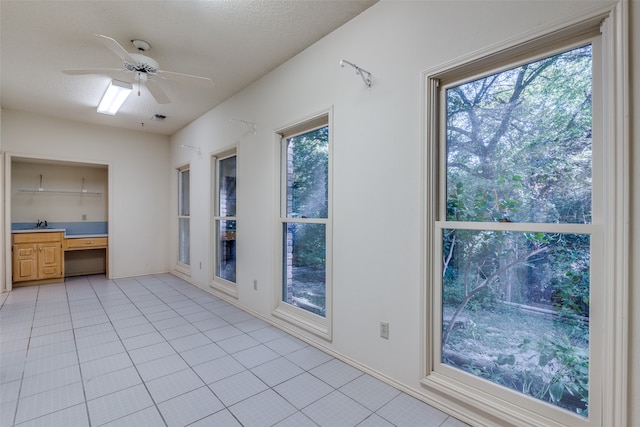 interior space with ceiling fan, multiple windows, built in desk, and light tile patterned floors