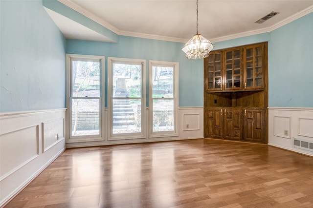 unfurnished dining area with visible vents, a wainscoted wall, and wood finished floors