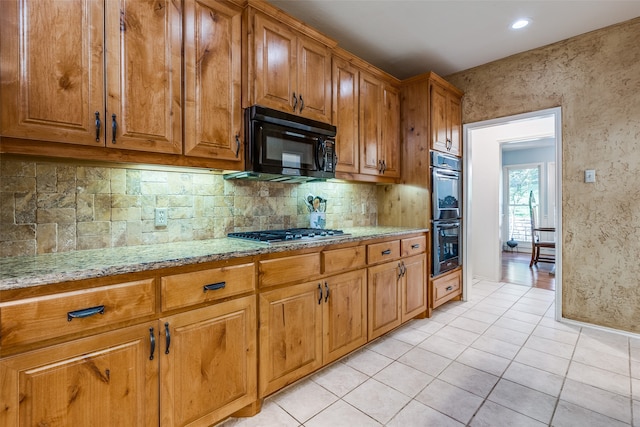 kitchen featuring decorative backsplash, light tile patterned floors, black appliances, and light stone counters